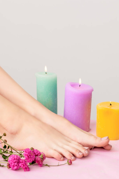 Mooie vrouwelijke benen blootsvoets versierd met brandende kaarsen en bloemen op witte achtergrond. - Foto, afbeelding