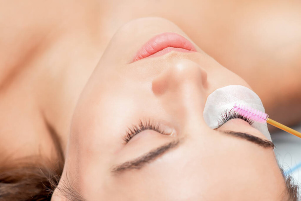 Woman receiving eyelash extension procedure with eyelash brush, close up. - Photo, Image