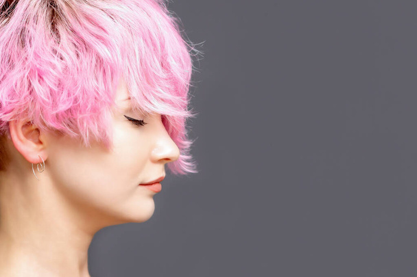 Femme avec coiffure rose debout sur fond gris, vue latérale avec espace de copie
. - Photo, image