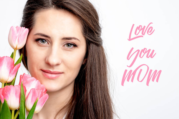 Love You Mom vaaleanpunainen teksti ja kaunis nainen vaaleanpunainen tulppaanit valkoisella taustalla. Äitienpäivän käsite
. - Valokuva, kuva