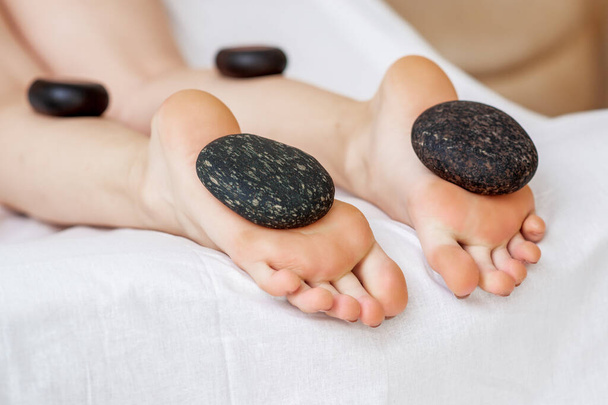 Hot stones liggend op voeten van vrouw tijdens voet massage op benen, close up. - Foto, afbeelding