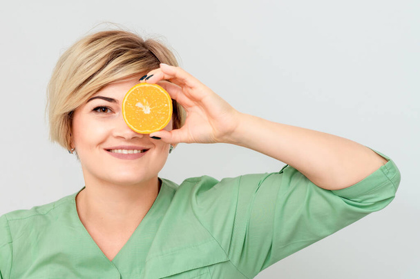 Cosmetologist is having piece of orange closing one eye isolated on white background. - Foto, Bild