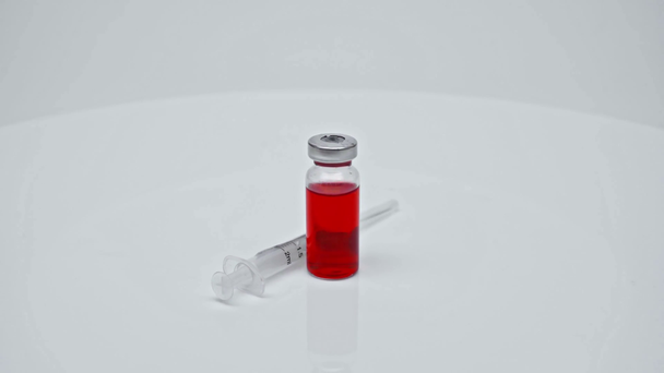 koronavirová červená vakcína a injekční stříkačka v laboratoři na bílém povrchu - Záběry, video