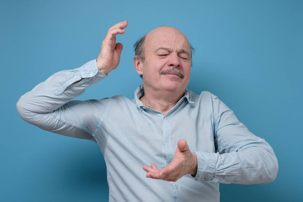 Hombre hispano mayor con camisa sudorosa debido a hiperhidrosis o clima caluroso. Estudio de tiro en la pared azul
. - Foto, imagen