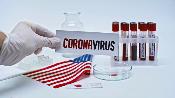 Laboratuvarda elinde coronavirus kartıyla Amerikan bayrağı taşıyan bir bilim adamı görüntüsü. - Video, Çekim