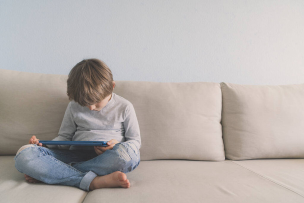 Young boy usina tablet on sofa at home - Zdjęcie, obraz