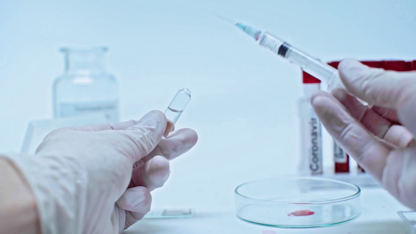 rajattu näkymä rokotetta ampullista ruiskussa keräävästä tutkijasta
 - Materiaali, video