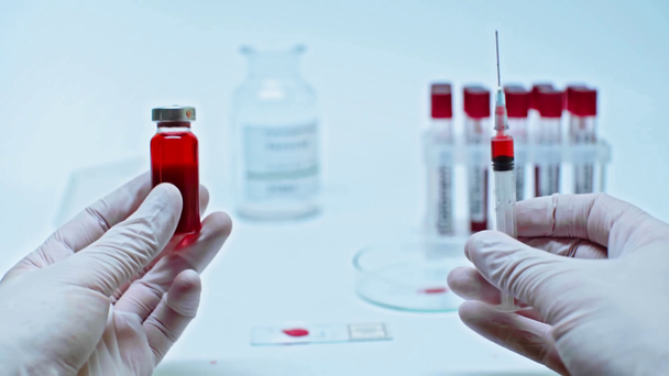 przycięty widok naukowca trzymającego strzykawkę i czerwoną szczepionkę - Materiał filmowy, wideo