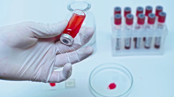 rajattu näkymä tutkijasta keräämässä punaista rokotetta ruiskussa
 - Materiaali, video