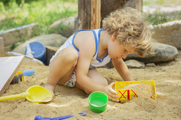 Милый ребенок играет в песочнице. Маленький мальчик играет во дворе
 - Фото, изображение