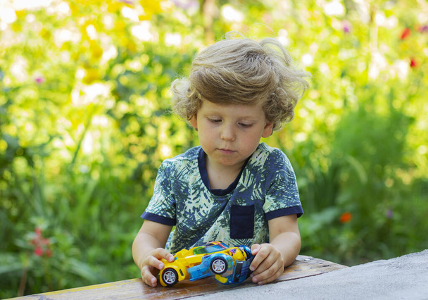 Mały chłopiec bawi się transformatorem na podwórku. Portret uroczego dziecka. - Zdjęcie, obraz
