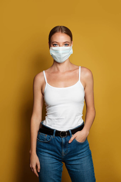 Woman wearing medical mask standing on vibrant yellow background - Foto, afbeelding