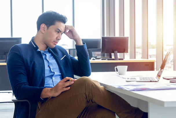 Ein junger Geschäftsmann sitzt in einem modernen Büro. Er hat das Gefühl, das Ergebnis nicht positiver Unternehmensgewinne gestresst zu sein. Auf seinem Tisch liegt ein Laptop-Tablet-Stift. - Foto, Bild