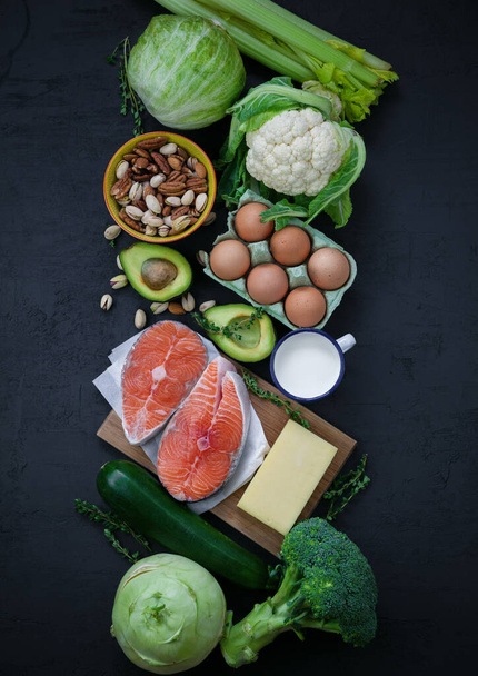 Az egészséges, kiegyensúlyozott étel termékei. Zöld zöldségek, avokádó, diófélék, lazac, tojás, tejtermékek. Egészséges étel koncepció. Rugalmas diéta, keto diéta. Fekete háttér, lapos laikus - Fotó, kép