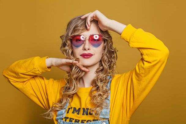 Young nice woman with long blonde curly hair on bright yellow background - Foto, afbeelding