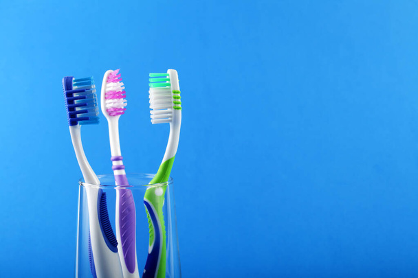 Three toothbrushes in a glass cup on a blue background, place for your text - Photo, Image