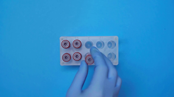 青色の背景に血液サンプルを用いた検査管を取る医師のトップビュー - 映像、動画