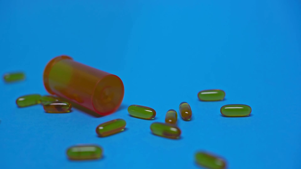 Enfoque selectivo del frasco rodando cerca de píldoras en superficie azul
 - Imágenes, Vídeo