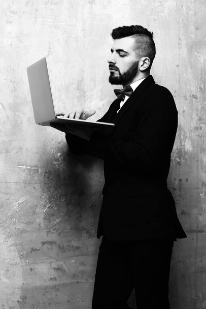 Attentive businessman with beard and fancy suit works on laptop - 写真・画像