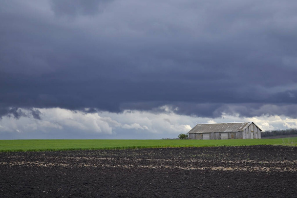 Eenzaam bouwen in een veld onder donkere donderwolken - Foto, afbeelding