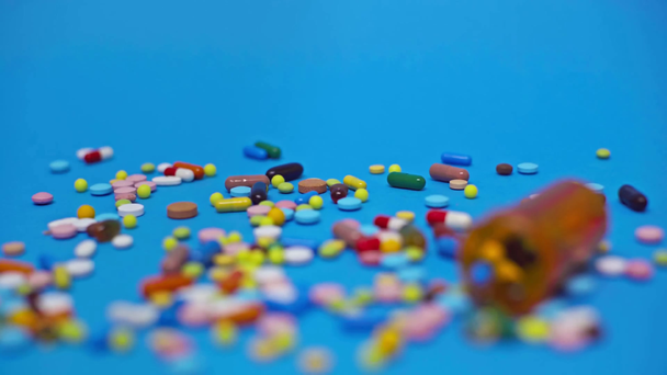 Selektywne skupienie słoika i kolorowych tabletek na niebieskim tle - Materiał filmowy, wideo