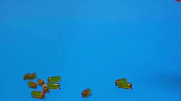 Zpomalený pohyb pilulek padající ze sklenice na modrém pozadí - Záběry, video