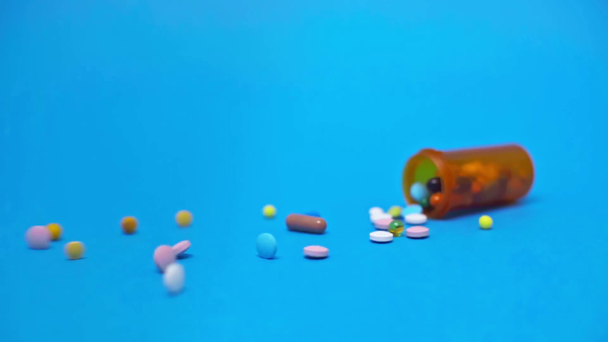 Zpomalený pohyb člověka házení sklenice s barevnými pilulky na modrém pozadí - Záběry, video