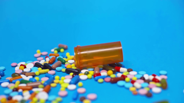 Slow motion of jar rolling on colorful pills on blue background - Filmati, video