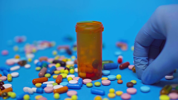 Cropped view of doctor putting pills in jar on blue background - Πλάνα, βίντεο
