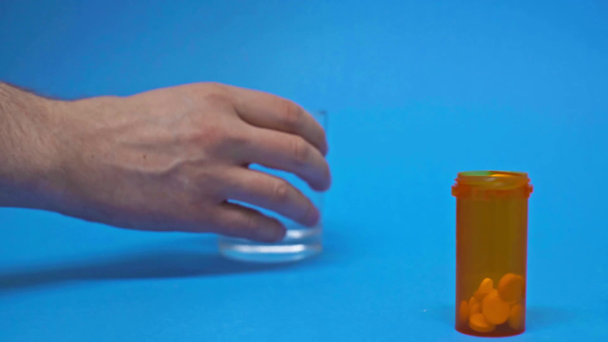 Обрезанный вид человека, принимающего таблетки и стакан воды на синем фоне
 - Кадры, видео