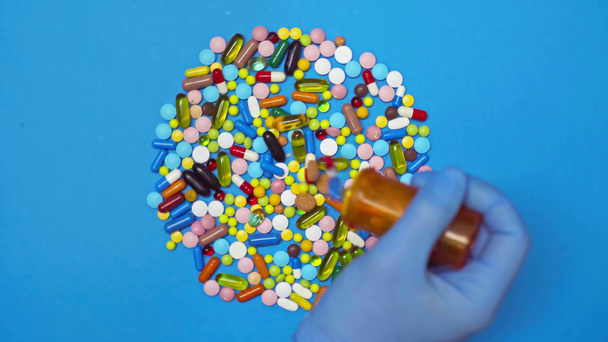 Top view az orvos üzembe tabletták jar a forgó kék háttér - Felvétel, videó