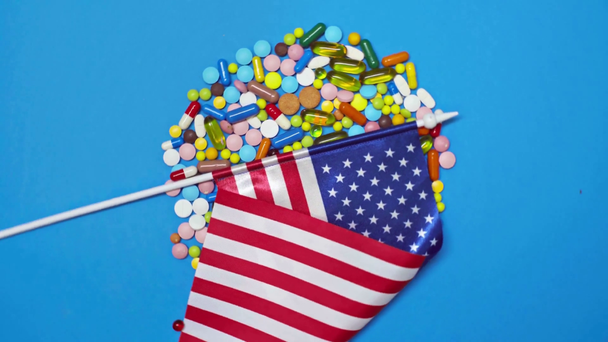 Widok z góry amerykańskiej flagi na pigułki na wirującym niebieskim tle - Materiał filmowy, wideo