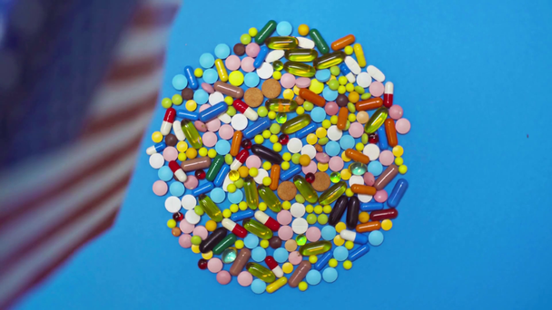 Selective focus of american flag and pills on spinning blue background - Metraje, vídeo