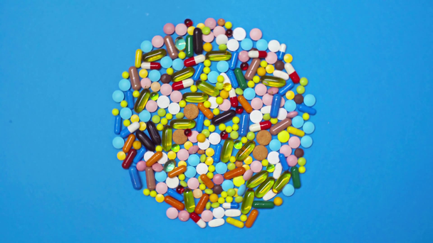 Vista superior del círculo de píldoras de colores sobre el fondo azul giratorio
 - Metraje, vídeo