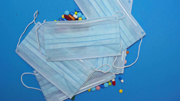 Vista superior del médico lanzando máscaras médicas en pastillas en la superficie azul giratoria
 - Metraje, vídeo