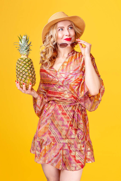 blonde woman holding pineapple in her hands on a yellow background in studio - Fotoğraf, Görsel