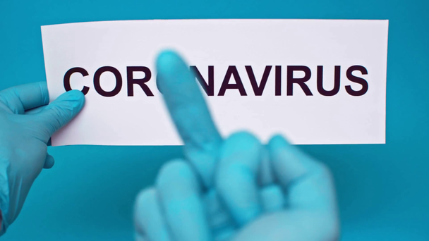 Mavi renkli Coronavirus kartının yanında orta parmağını gösteren bir adam görüntüsü. - Video, Çekim