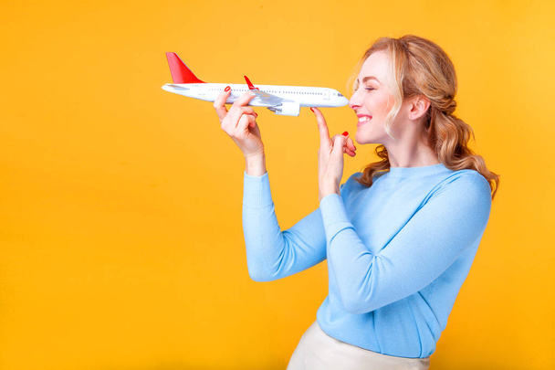 blonde woman holding a white plane in her hands on a yellow background in the studio - Foto, immagini