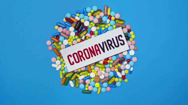 Vista superior de la tarjeta con letras coronavirus en píldoras sobre fondo azul giratorio
 - Metraje, vídeo