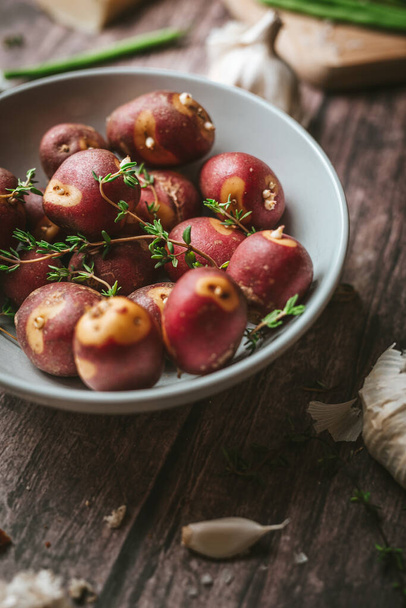 Kırmızı patateslere yakın plan biberiye, baharat, sarımsak, fasulye kabukları mutfakta kırsal ahşap bir masa üzerinde dikey - Fotoğraf, Görsel