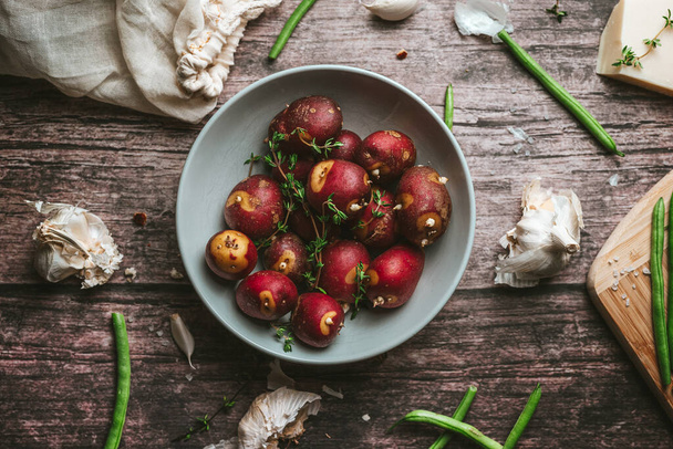 Flat lay of red potatoes with rosemary and spices, garlic, bean pods on a rustic wooden table in the kitchen - Fotoğraf, Görsel