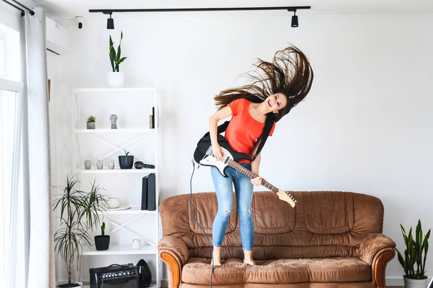 woman with an electric guitar dances on a sofa - Фото, зображення