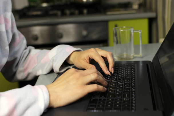 young woman in pyjamas works on a laptop in the kitchen. Freelance business quarantine concept, remote work at home - Fotografie, Obrázek