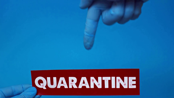cropped view of man pointing at red card with quarantine word isolated on blue - Imágenes, Vídeo