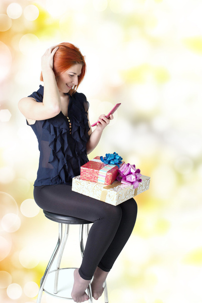 Happy girl on a chair with a telephone and a gift box - Фото, изображение