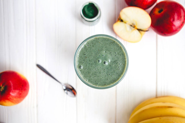 The concept of food and drink, diet and nutrition. Healthy green vegan smoothie with banana, spirulina and ripe apple for summer detoxification - Fotografie, Obrázek