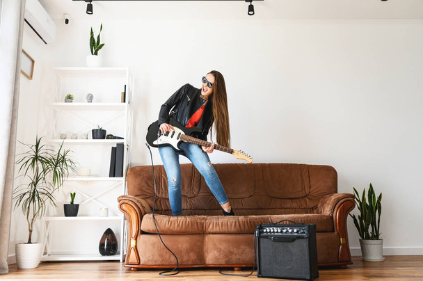 A woman with an electric guitar dances on a sofa - Фото, изображение
