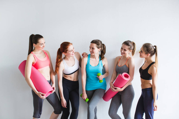 Group of young sporty woman with yoga mats standing at white wall. Female in gym after fitness. - Photo, Image