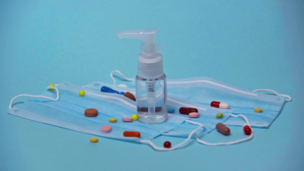 pills falling on bottle with sanitizer and medical masks on blue - Footage, Video