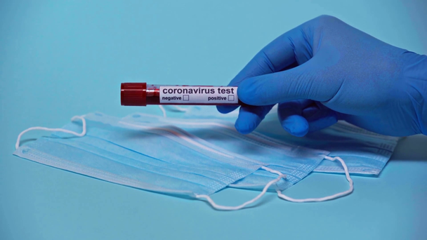 Ausgeschnittene Ansicht eines Arztes mit Coronavirus-Probe in der Nähe medizinischer Masken auf blau  - Filmmaterial, Video